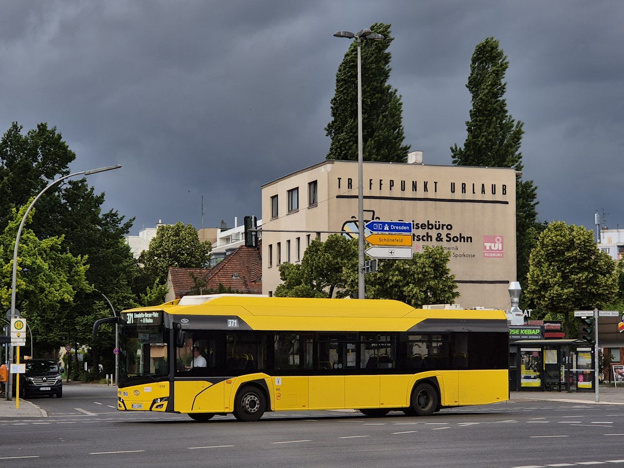 gallery-2 Yellow city bus crossing intersection in Berlin with stormy sky and travel agency background.